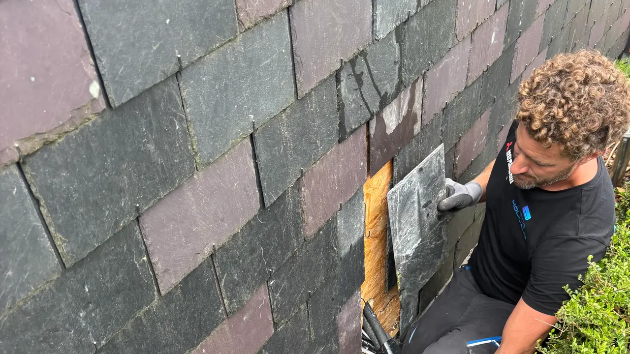 Rein zet een leisteen terug in de donkere leien gevel, waar de zwarte leidingen naar binnen gaan.