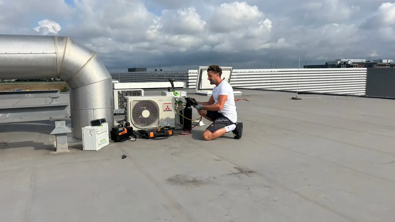 Rein meet aan een buitendeel op een plat dak, met gereedschap en koffers om zich heen.
