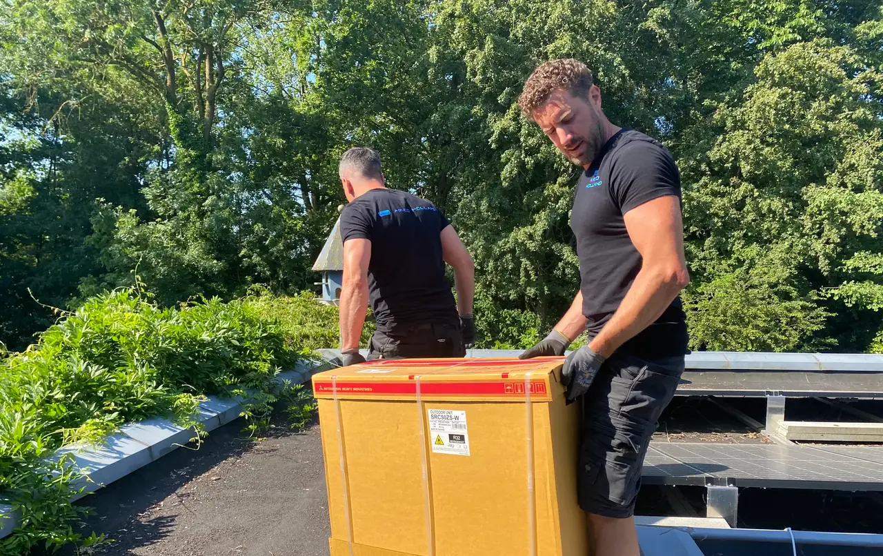 Peter en Rein tillen samen een buitendeel in de doos over een plat dak, met bomen eromheen.