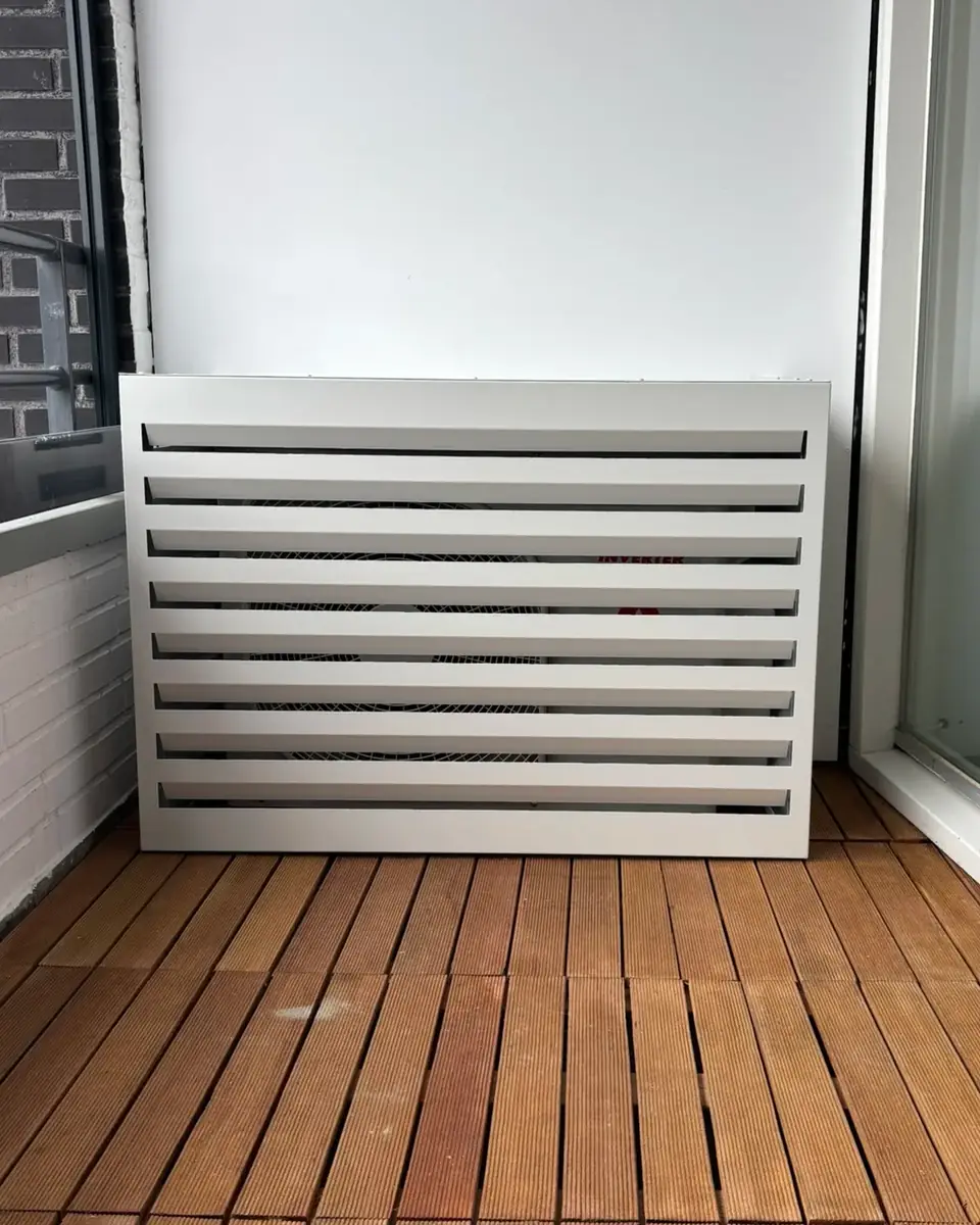 Een buitendeel in een witte lamellenkast op het balkon van een appartement, op een houten vloer.